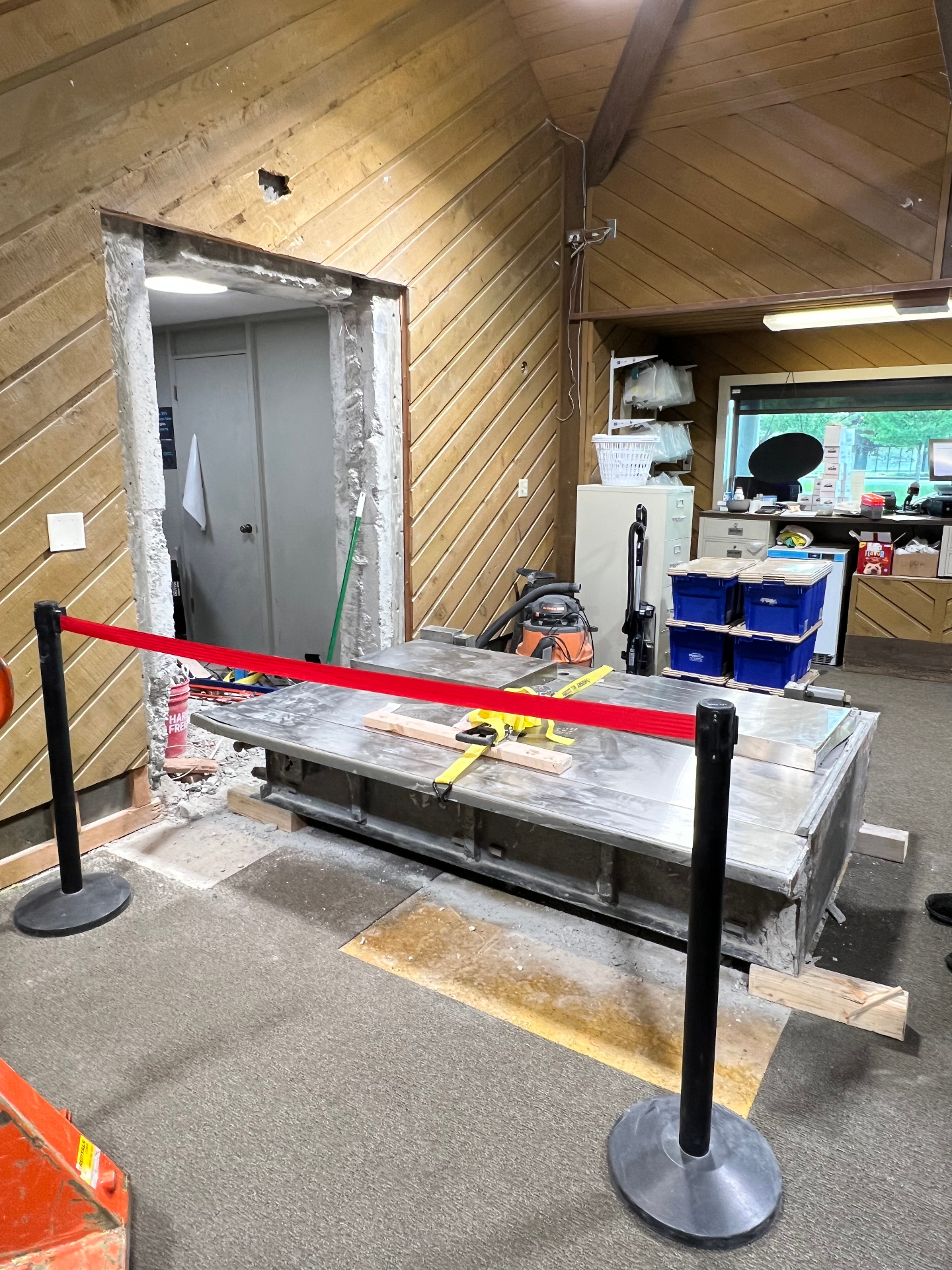 Interior commercial demolition with a wall opening cut through and heavy equipment staged for removal